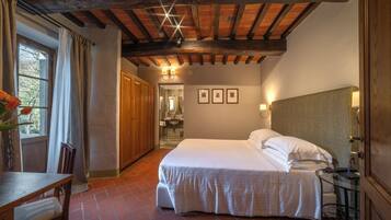 Una camera da letto con un letto grande, travi in legno a soffitto, una finestra con tende, una scrivania in legno e un comodino con una lampada.