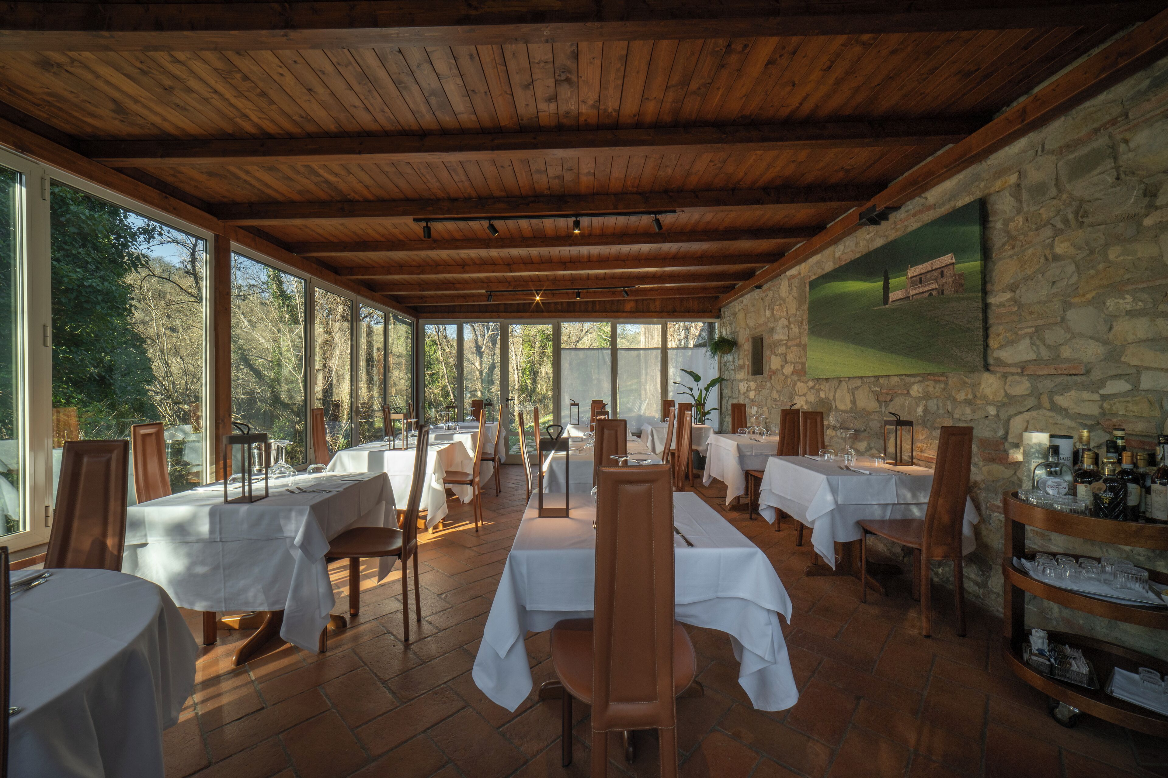 Un restaurante con vigas de madera y paredes de piedra, con mesas dispuestas para comer y vistas al exterior.