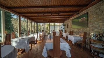 Un restaurante con vigas de madera y paredes de piedra, con mesas dispuestas para comer y vistas al exterior.
