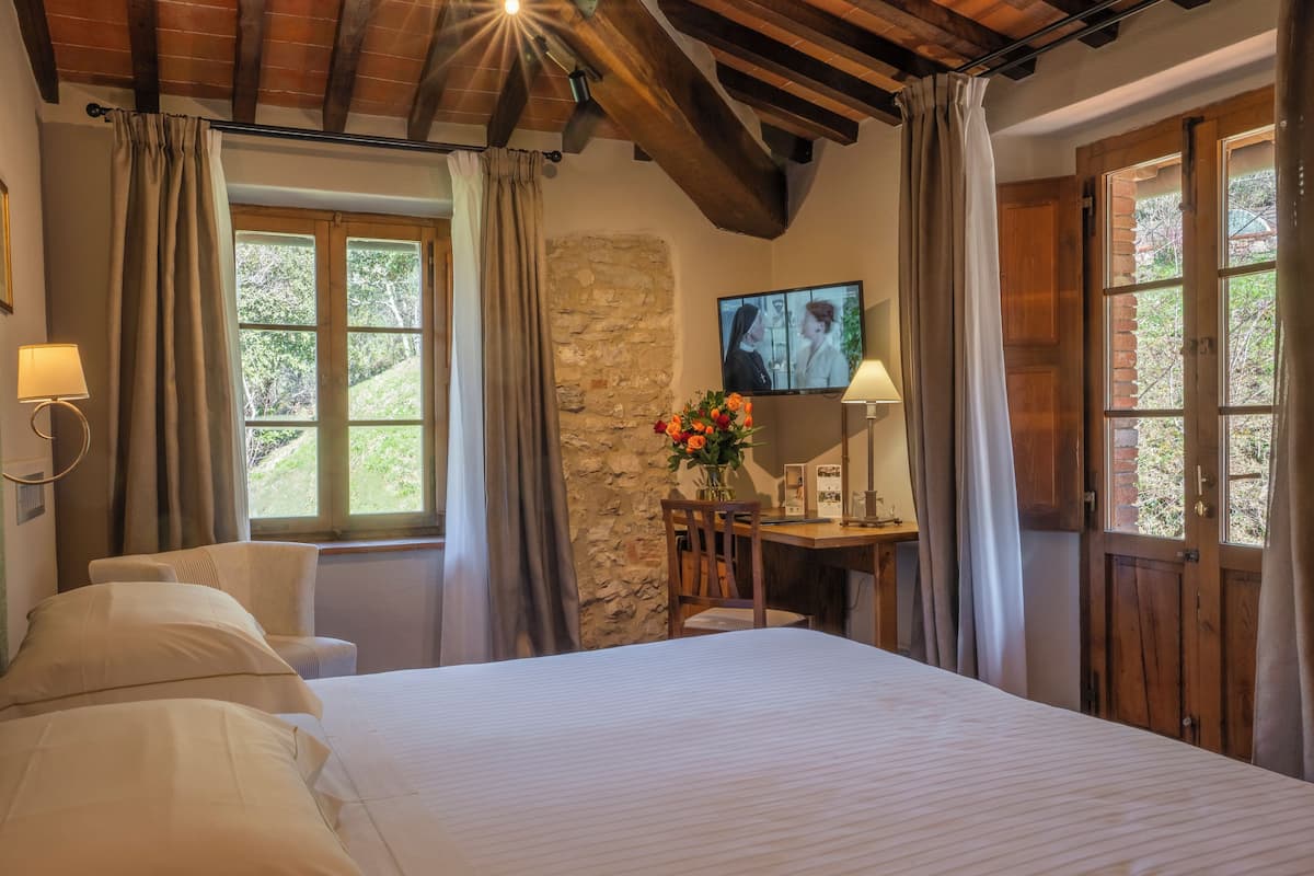 Un dormitorio con una cama grande, un escritorio con lámpara, una silla y una pared de piedra.