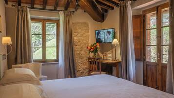 Une chambre avec un grand lit, un bureau avec une lampe, une chaise et un mur en pierre.