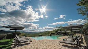 A poolside area with lounge chairs and umbrellas, surrounded by stone flooring and greenery. - Ultimo Mulino Wellness Country Hotel (Gaiole in Chianti)