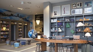 Un vestíbulo de hotel moderno con un mostrador de recepción de madera, varios taburetes de bar, un gran globo decorativo y una pared con cuadros enmarcados y estantes que exhiben diversos objetos.