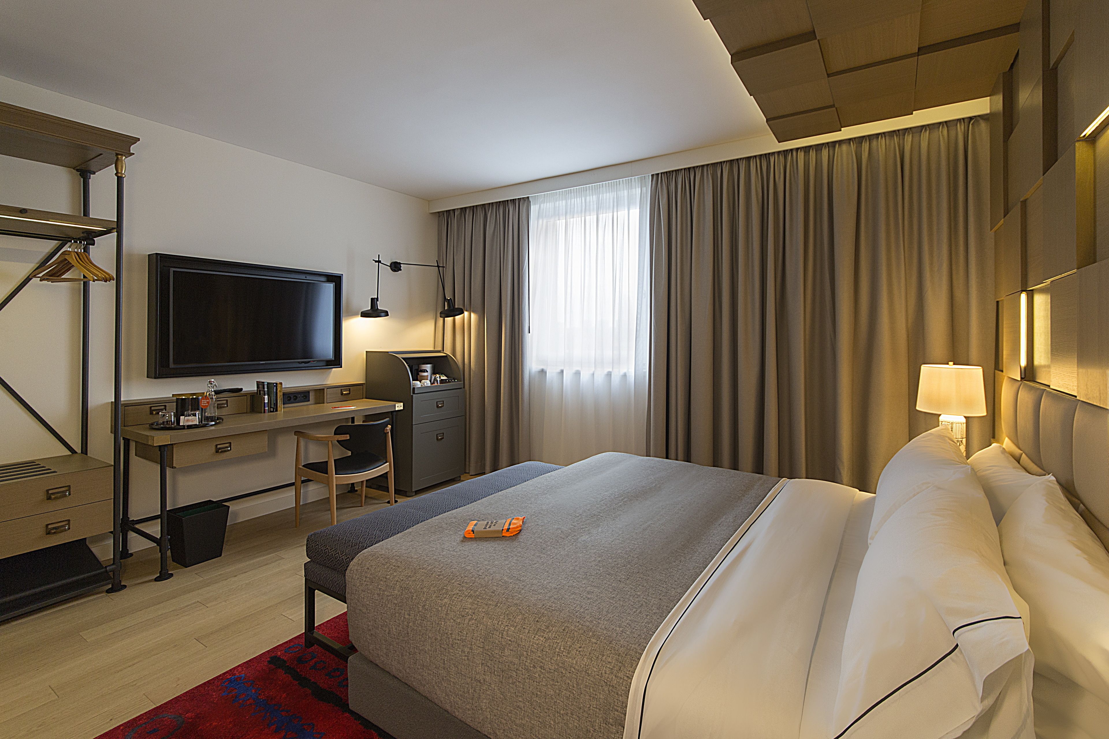Una habitación de hotel con cama, escritorio, silla, televisor y cortinas.