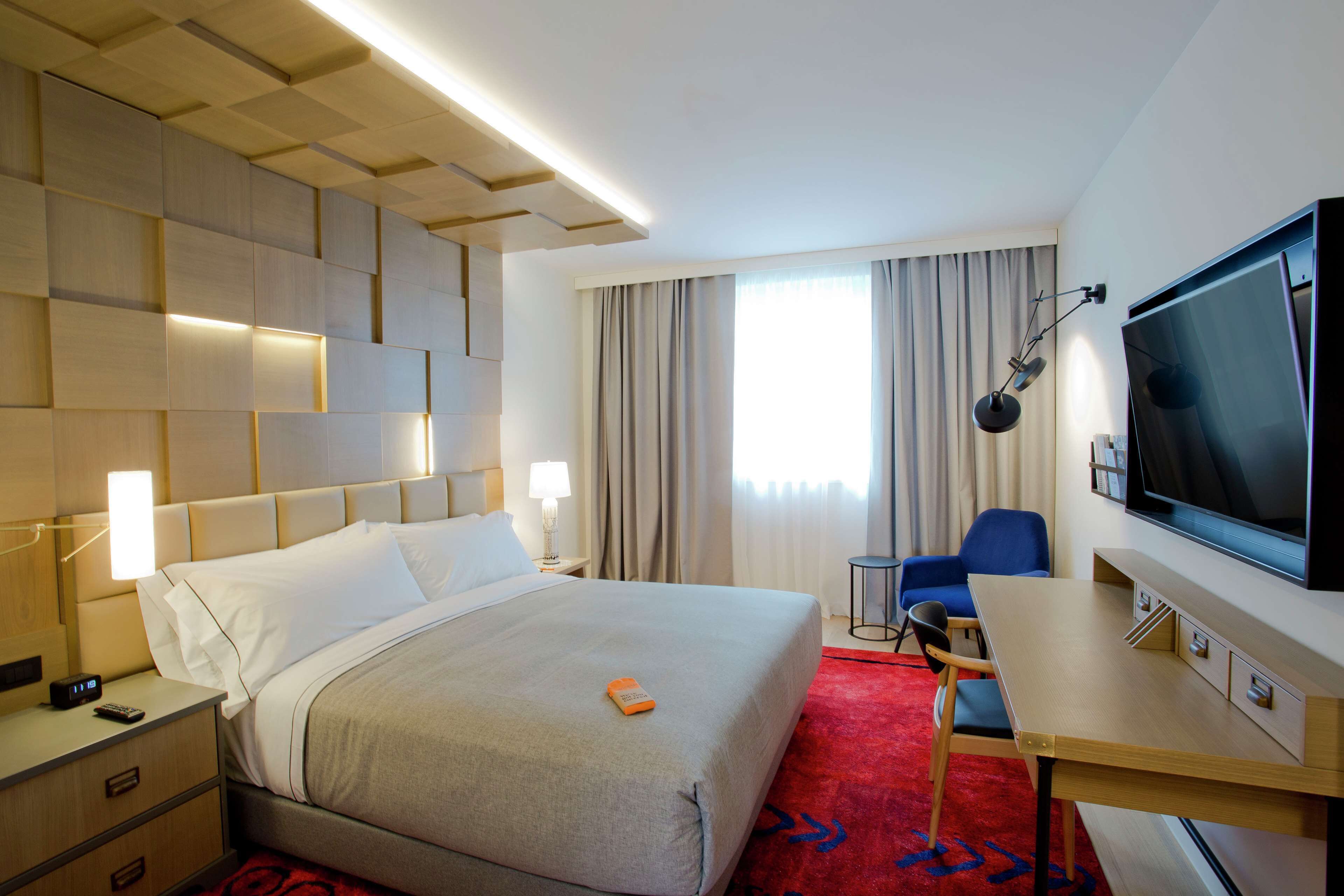 Habitación de hotel con una cama grande, mesitas de noche, un escritorio con televisor y una silla.