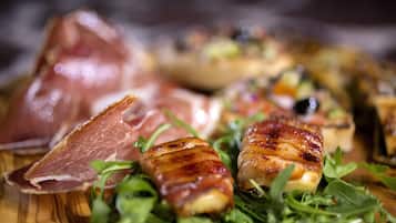 Una mesa de madera con diversos alimentos, incluyendo un trozo de carne y algunos adornados con hojas verdes.