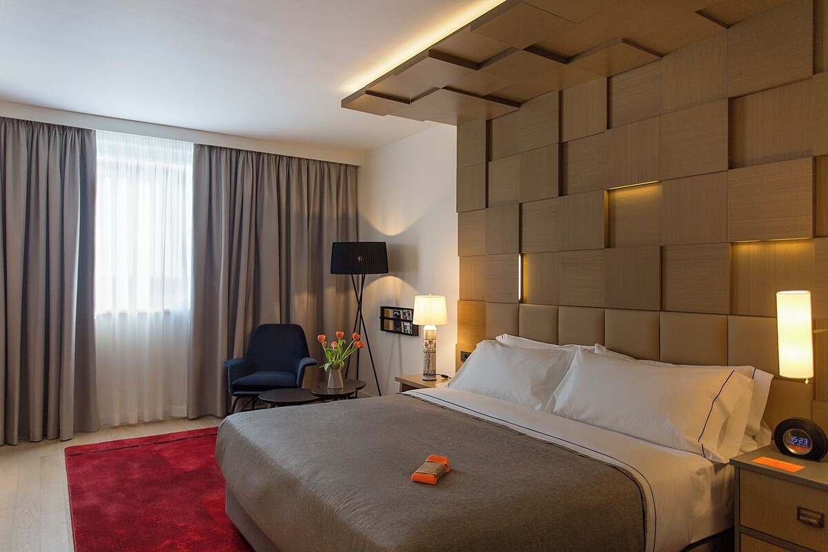 A hotel room with a large bed, a chair, a desk, and a TV.