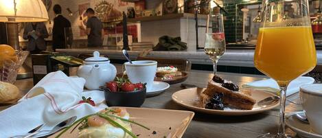 A dining table with breakfast items including eggs, toast, and fruit. There are also wine glasses and a bottle of orange juice.