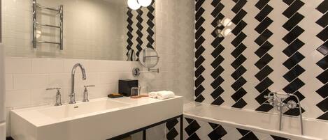 A modern bathroom with a large white sink, two faucets, a mirror, and a black and white patterned shower wall.