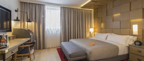 Habitación de hotel con una cama, mesitas de noche, un escritorio con una silla, un televisor y una ventana con cortinas.
