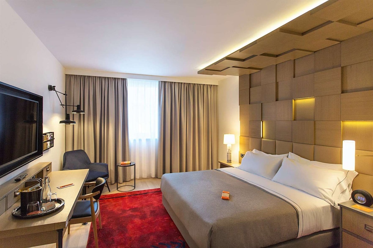 Una habitación de hotel con cama, escritorio, televisor y cortinas.