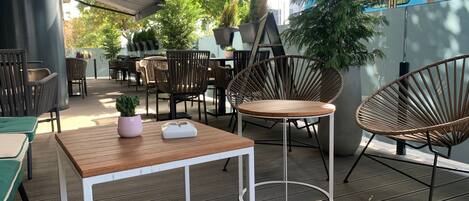 An outdoor seating area with tables and chairs, a small table with a plant and a white object, and a large potted plant.