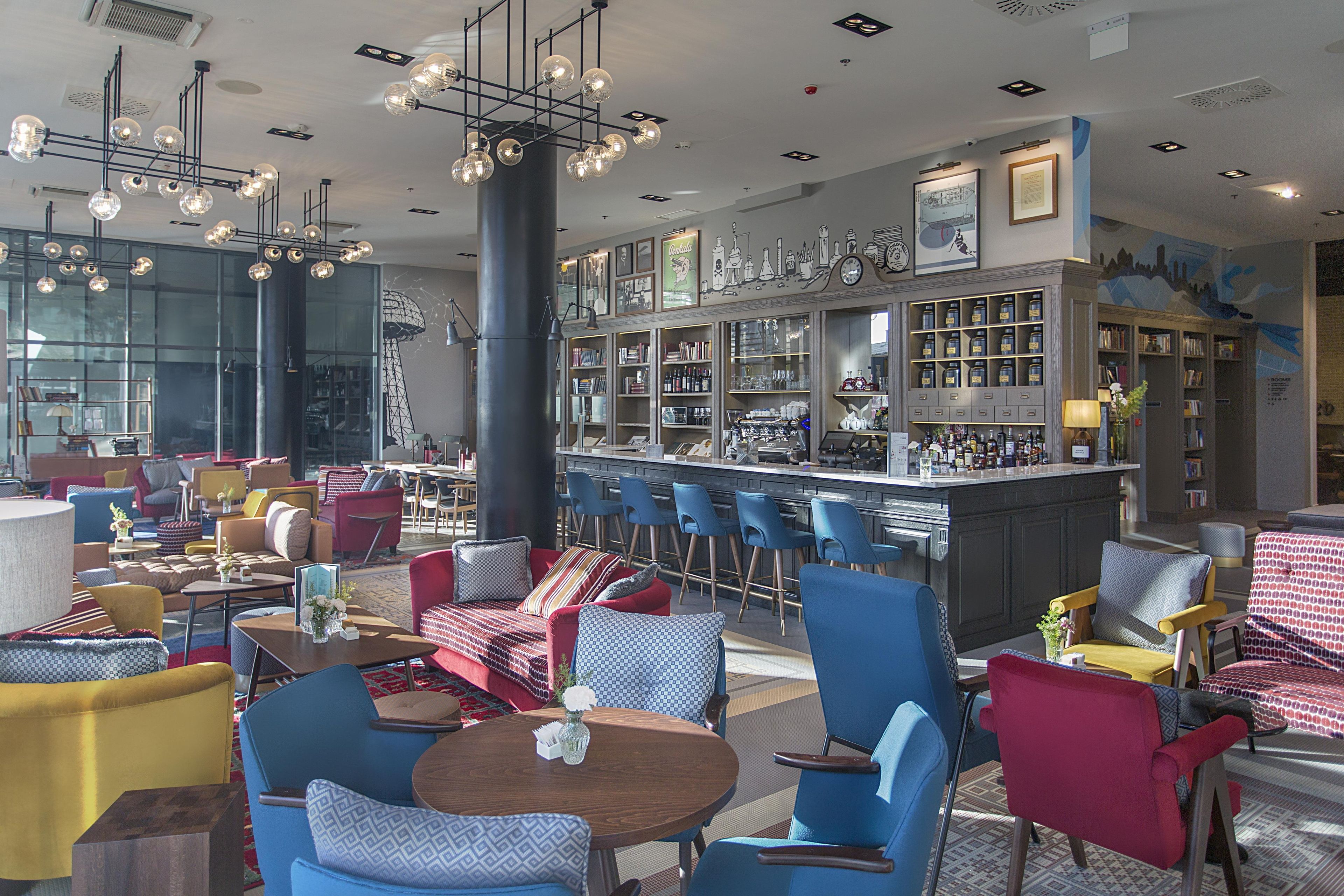 A bar area with a variety of seating options including round tables and bar stools, a bar counter with a display of bottles, and a wall with framed pictures and a cityscape mural.
