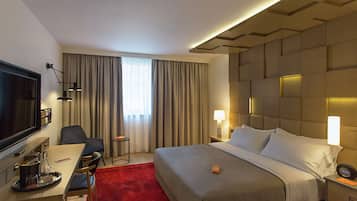 A hotel room with a bed, a desk with a chair, a TV, and a red carpet.