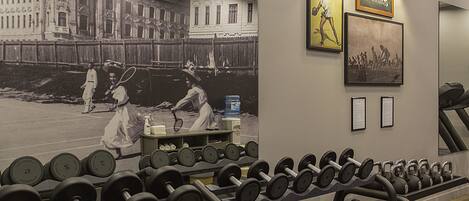 A gym with a wall mural, dumbbells, and exercise equipment.
