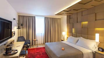 Habitación de hotel con una cama grande, un escritorio con silla, un televisor y una alfombra roja.