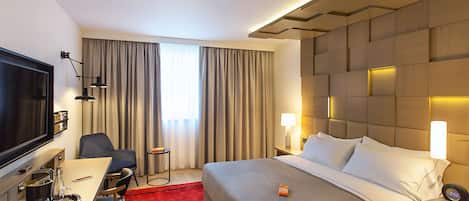 Habitación de hotel con una cama grande, un escritorio con silla, un televisor y una alfombra roja.