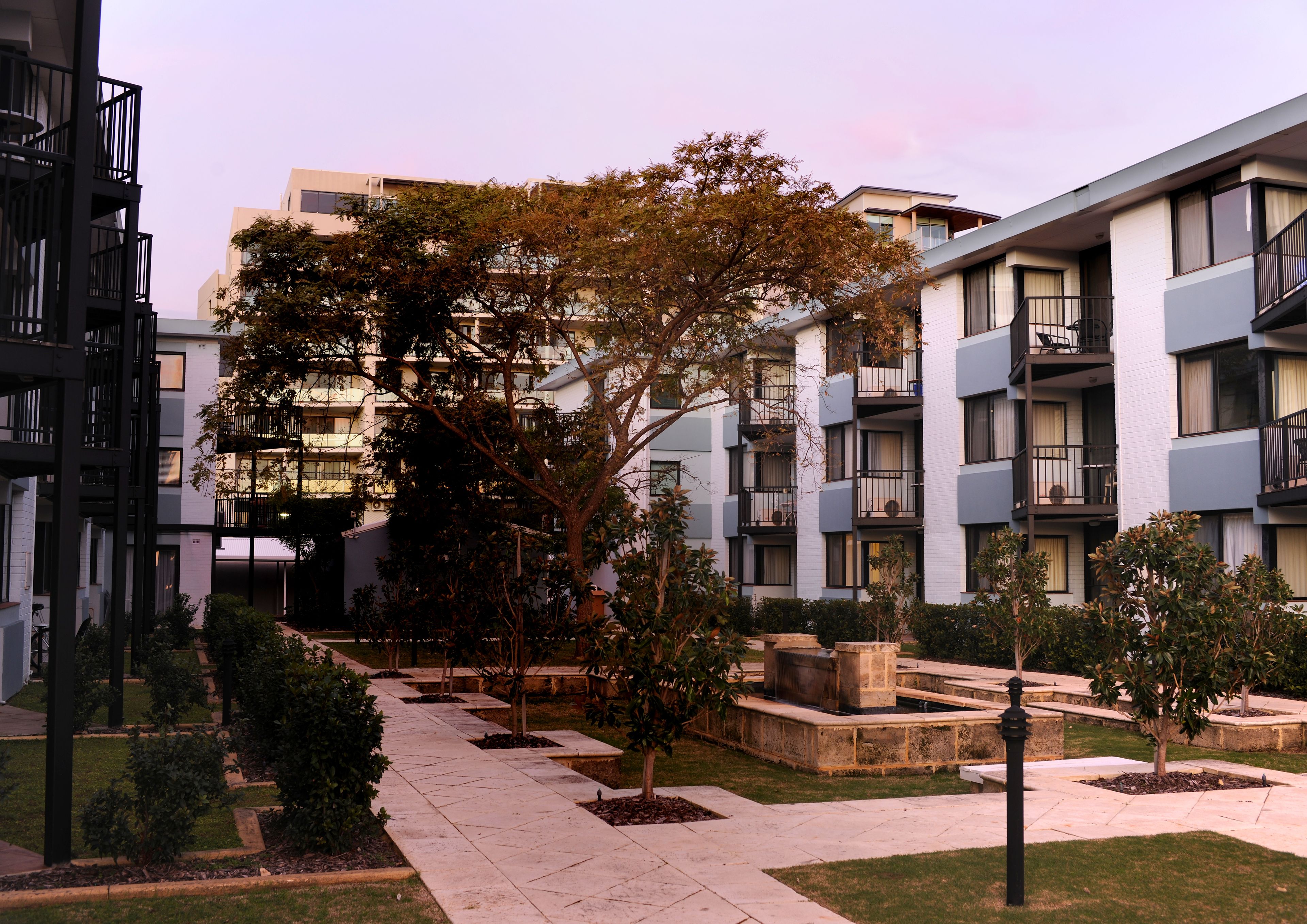 A modern apartment building with balconies, a central courtyard with trees, and a bike parked outside.
