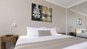 Une chambre d’hôtel avec un grand lit, une table de chevet, une commode et une œuvre d’art accrochée au mur.