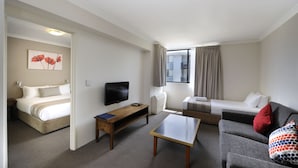 Une chambre d’hôtel avec un lit, un canapé, une table basse, une télévision et une fenêtre avec des rideaux.