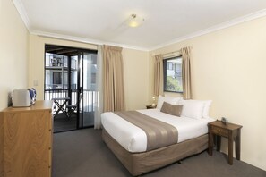 Ein Hotelzimmer mit einem großen Bett, einem Holztisch, einem Stuhl, einem kleinen Tisch und einem Balkon mit Geländer.