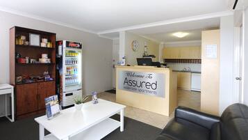 A reception area with a white desk, a vending machine, and a sign welcoming to Assured Waterside Apartments.