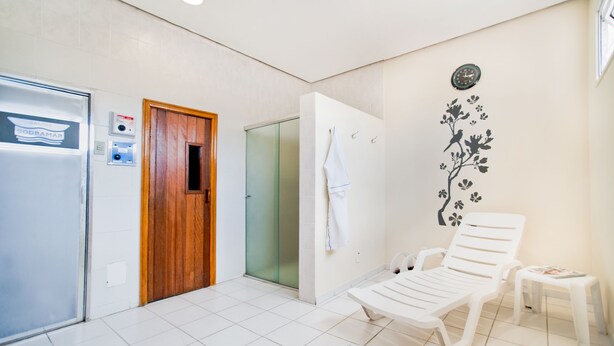 Un bagno con doccia, portasci, orologio e una sedia bianca.