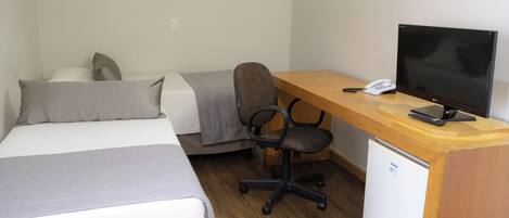Habitación de hotel con cama, escritorio con ordenador, silla y un pequeño refrigerador.