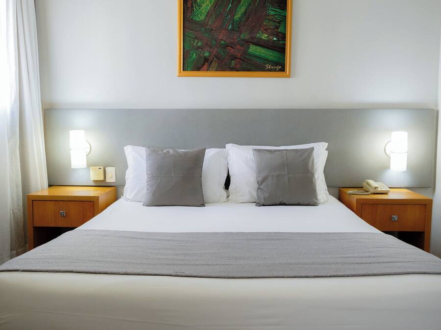 A hotel room with a bed, two bedside tables, a painting, and a nightstand with a telephone.