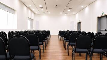 A conference room with rows of black chairs, wooden flooring, white walls, and ceiling lights.