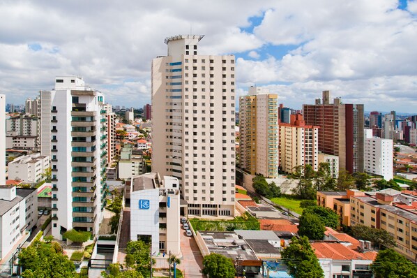 Un edificio alto con varios pisos y balcones, rodeado de otros edificios y vegetación.
