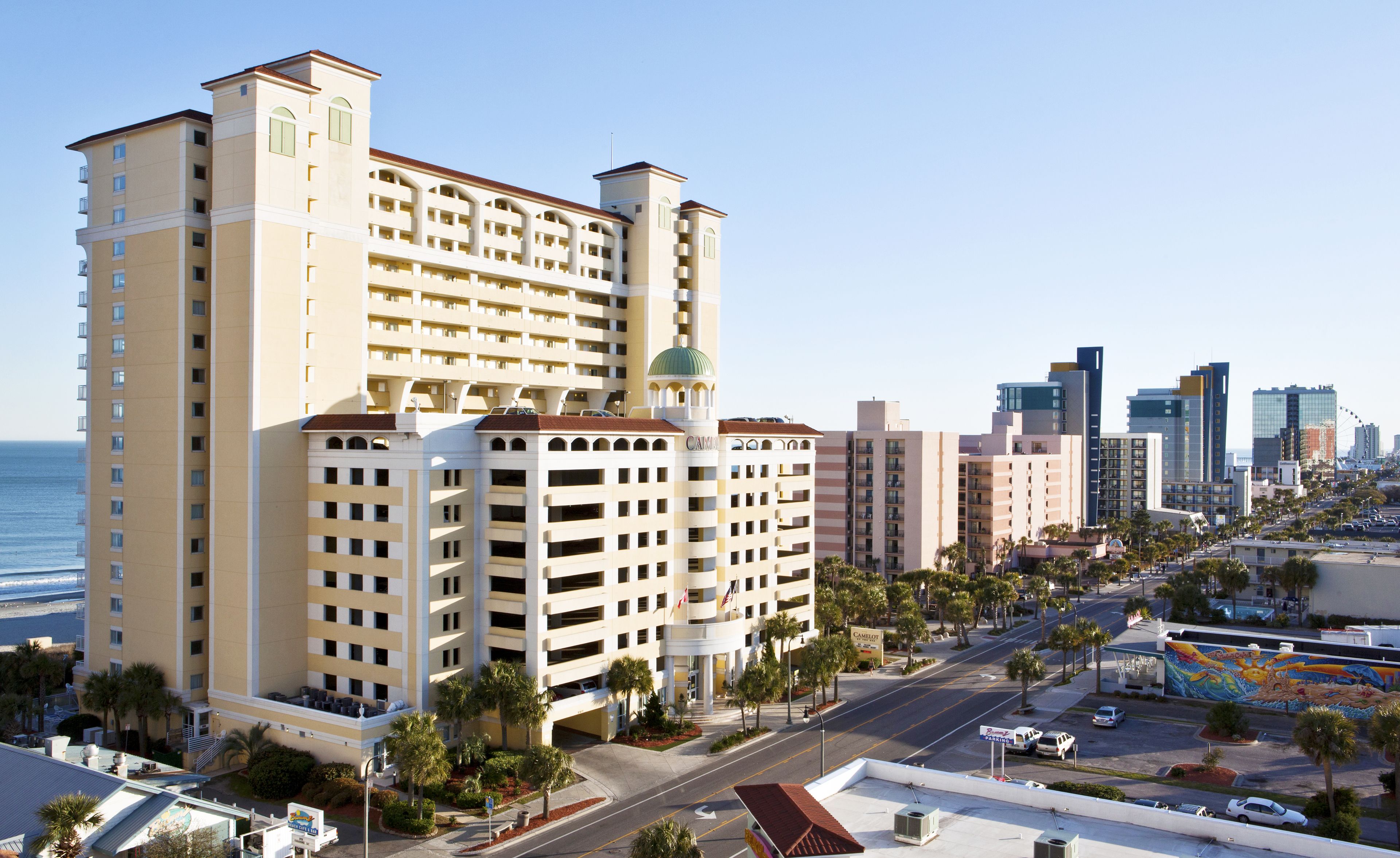 A multi-story hotel with a central courtyard, parking facilities, and a view of the ocean.