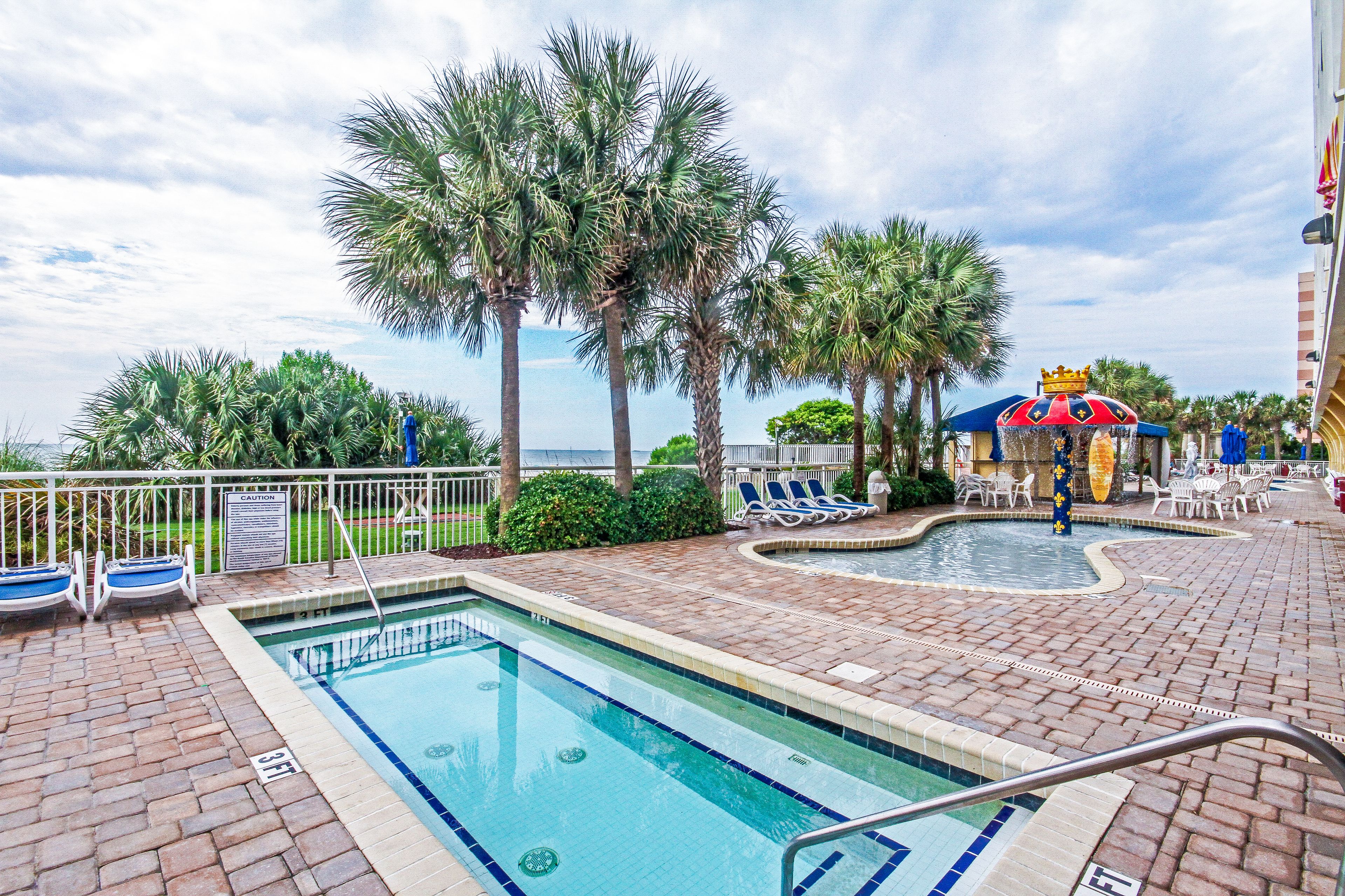 A pool area with a clear view of the ocean, palm trees, and lounge chairs.