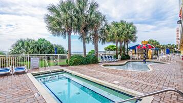 A pool area with a clear view of the ocean, palm trees, and lounge chairs.