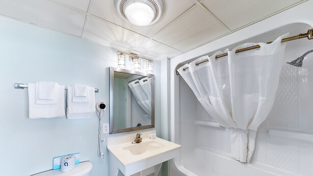A bathroom with a toilet, sink, mirror, and bathtub. - Camelot By The Sea by Oceana Resorts (Myrtle Beach)