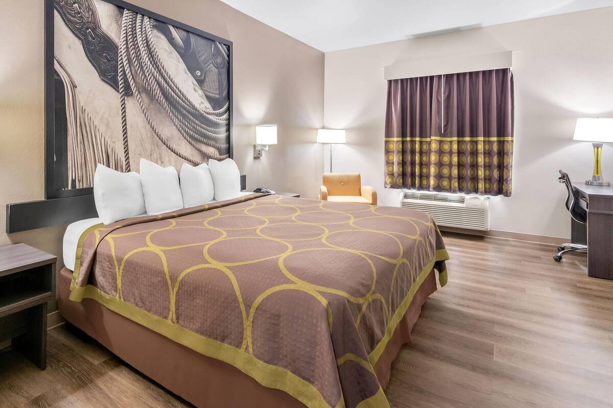 A hotel room with a large bed, a desk, a chair, a large painting on the wall, and a window with curtains.