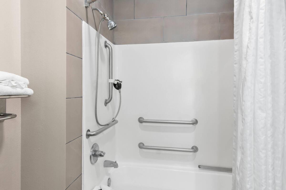 A bathroom with a white bathtub, grab bars, a showerhead, and a towel rack.