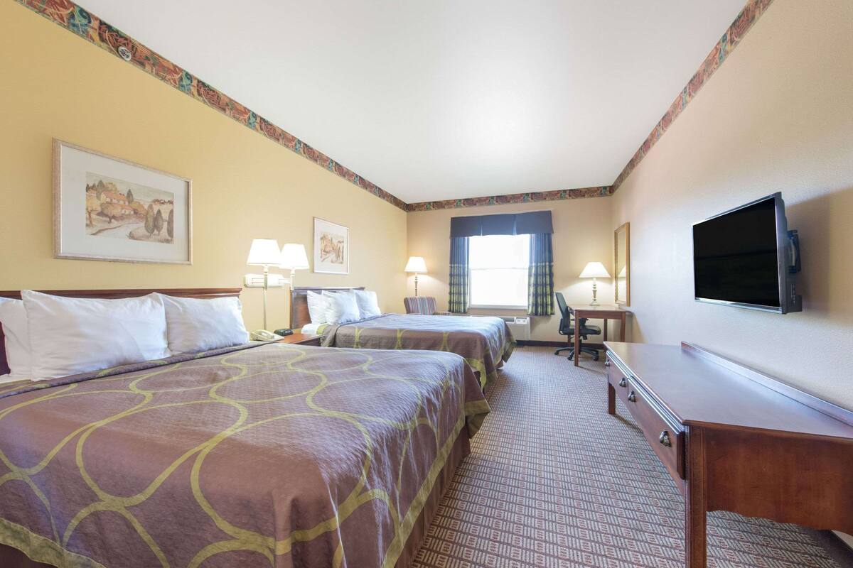 A hotel room with two beds, a desk, a television, and a window with curtains.