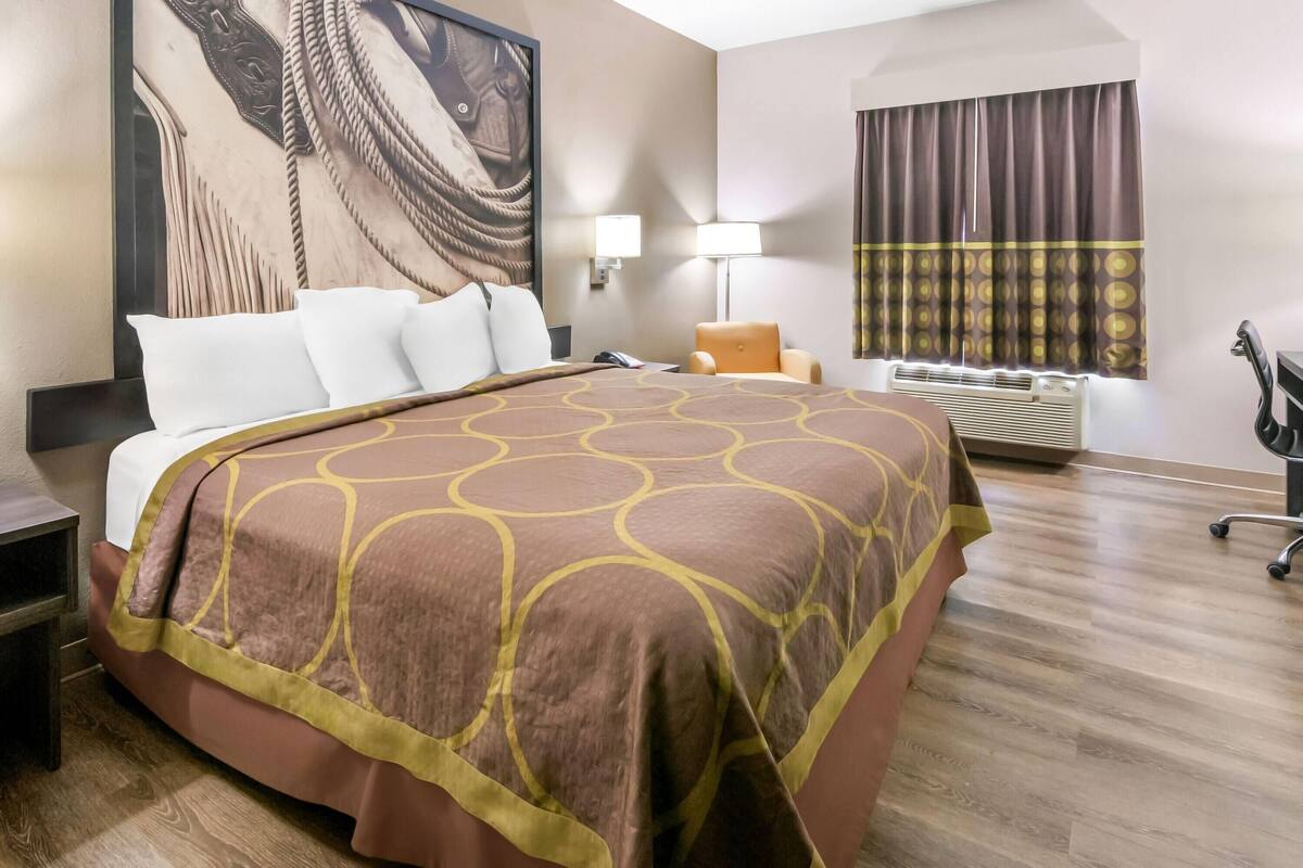 A hotel room with a large bed, a desk, a chair, a lamp, and a window with curtains.