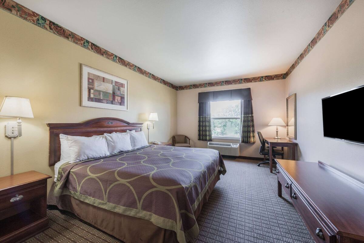 A hotel room with a bed, two bedside tables, a desk, a chair, a TV, and a window with curtains.
