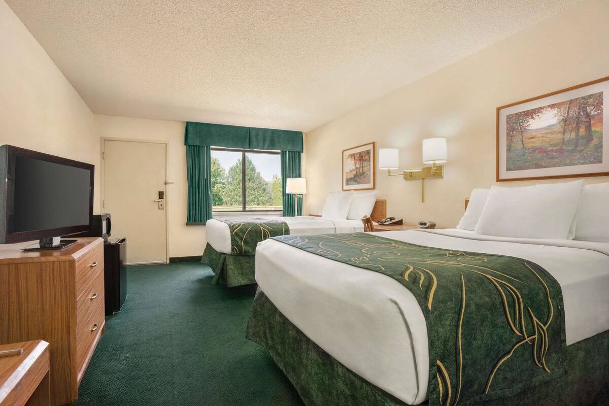 A hotel room with two beds, a TV, a desk, and a window with curtains.