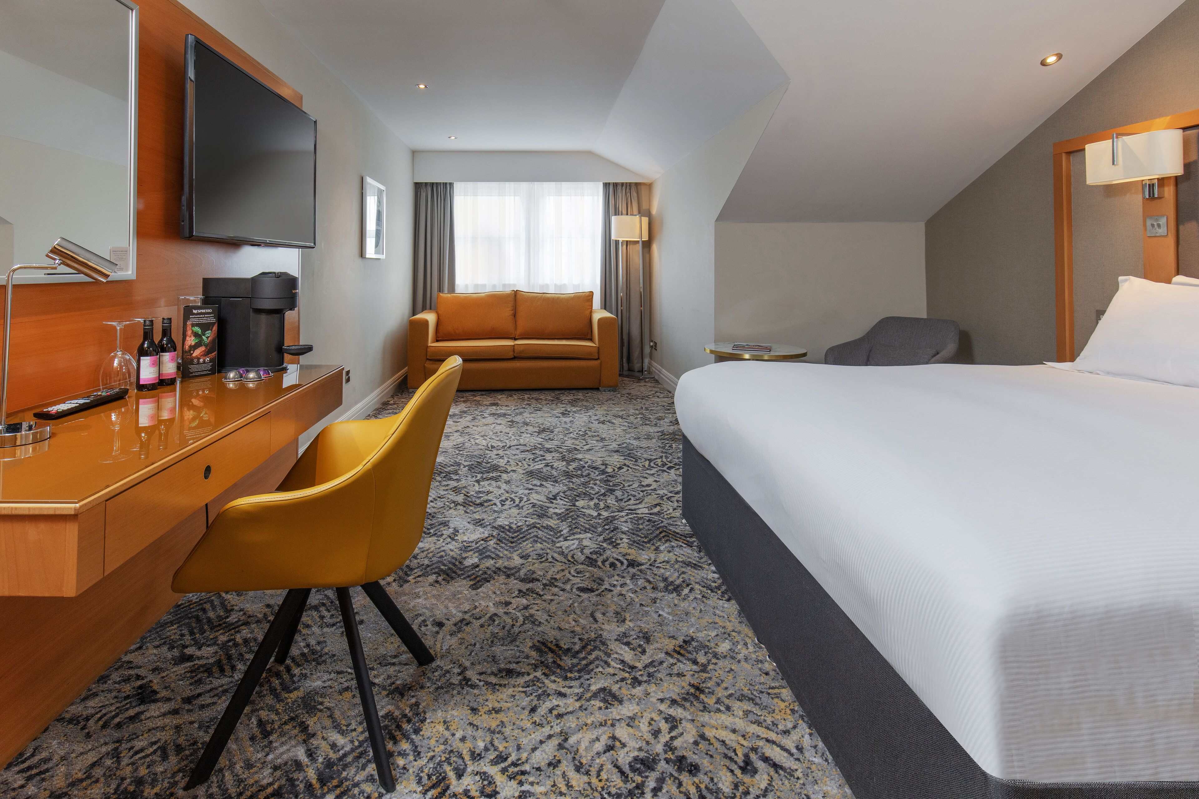 A hotel room with a bed, a desk with a coffee maker, a sofa, and a TV.