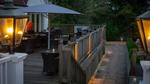 An outdoor patio with wooden railings, wicker furniture, and table lamps. - Chesford Grange Hotel (Kenilworth)