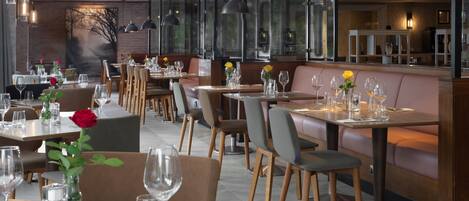 En restaurang med många bord och avskilda sittplatser, där varje bord är dukat med vinglas och blommor.