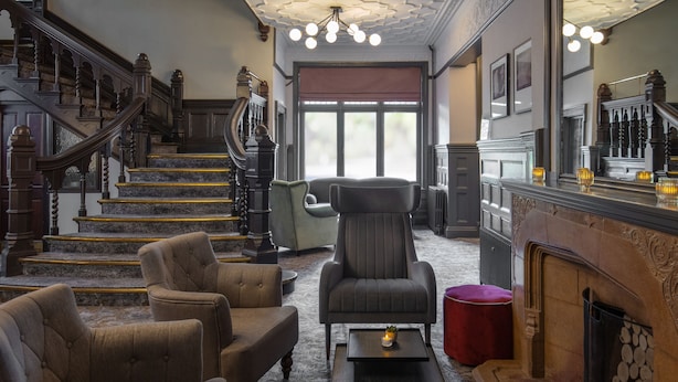 A grand staircase leading to a landing with a fireplace, a seating area with armchairs, and a large window with a view. - Chesford Grange Hotel (Kenilworth)