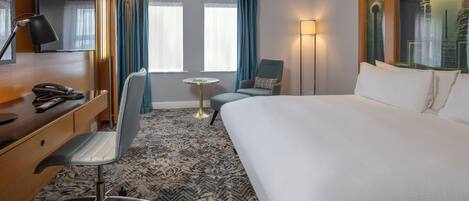 Una habitación de hotel con una cama grande, un escritorio con teléfono, una silla, una mesita redonda y un espejo amplio.