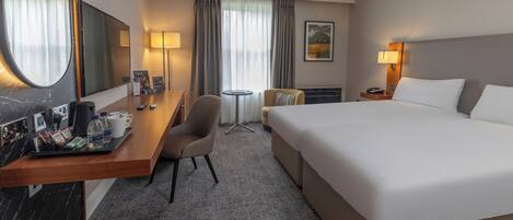A hotel room with a large bed, a desk with a chair, a small table, and a mirror.