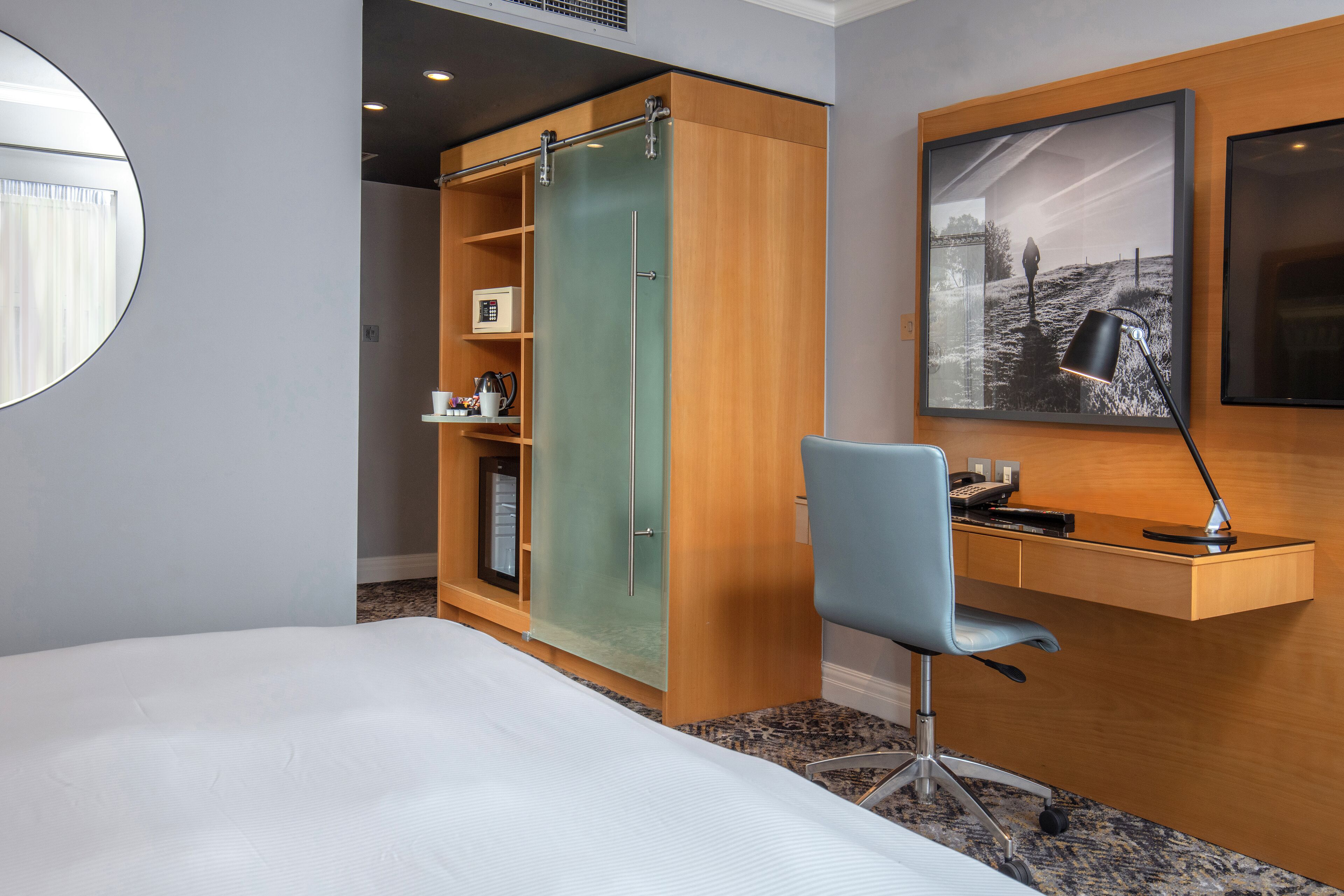 Een hotelkamer met een bed, een bureau met stoel, een kledingkast en een ingelijst foto aan de muur.
