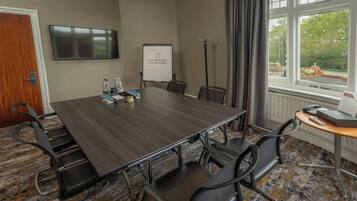 A conference room with a long table, chairs, a whiteboard, a TV, and a window with a view of greenery.
