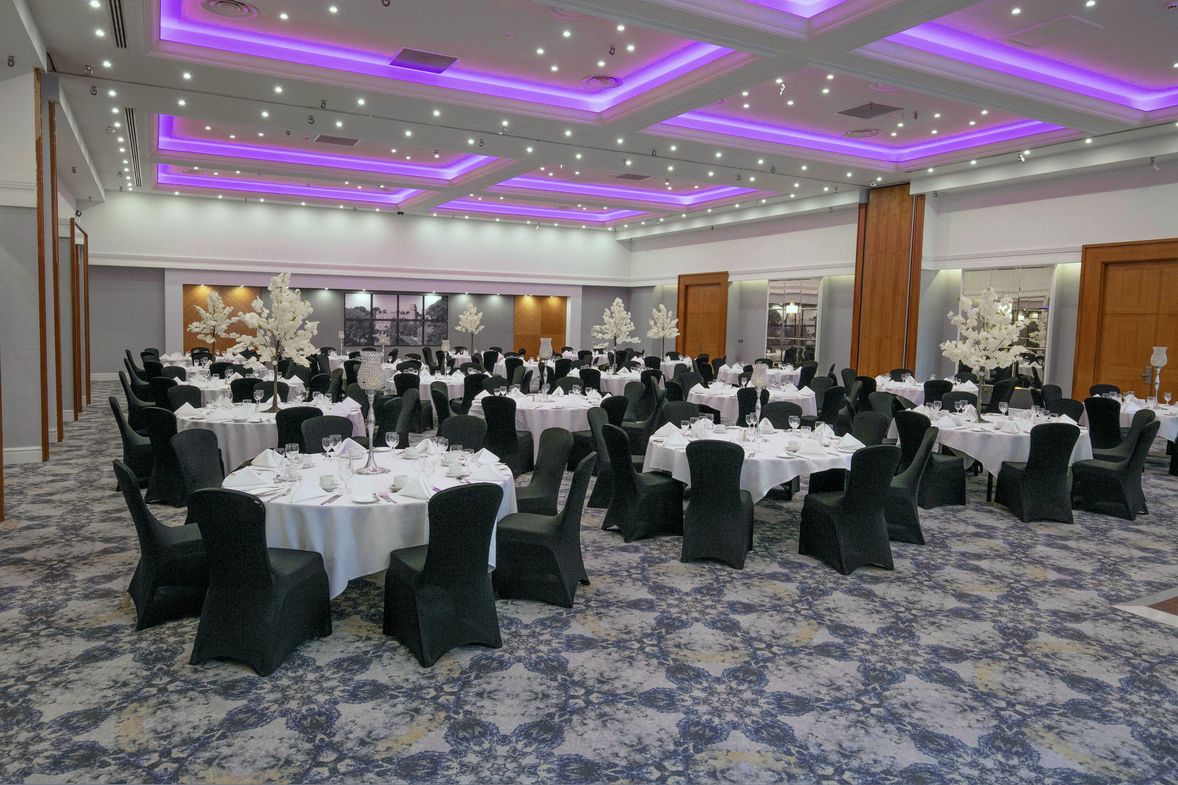 A banquet hall with round tables, black chairs, and white tablecloths.